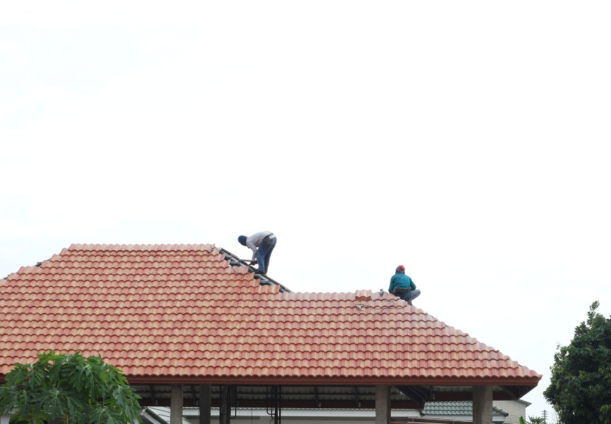 Two roofers working on a tile roof replacing tile shingles
